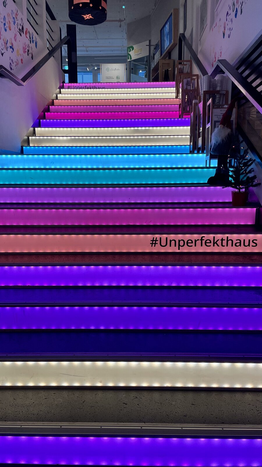 Bunte Treppenstufen beleuchtet mit Neonlicht und der Aufschrift #Unperfekthaus.