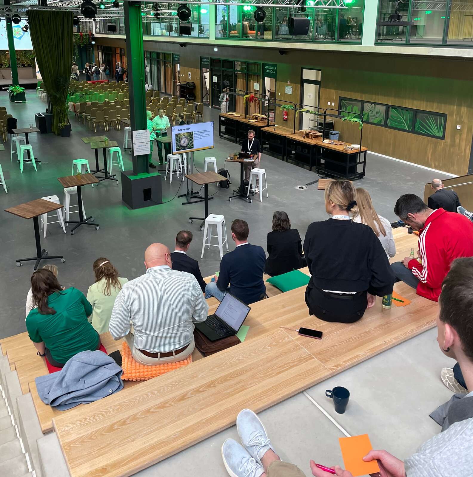Teilnehmende des Workshops bei der OER im Blick 2026 sitzen auf Tribüne, während Phillip unten steht und das FOERBICO-Projekt präsentiert.